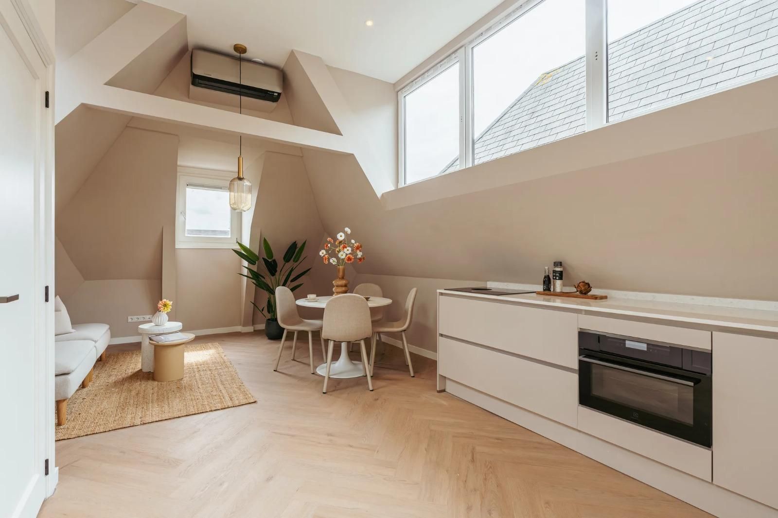 Lichte houten vloer in een studio-appartement met keukenblok, eethoek en zithoek onder een dakkapel.