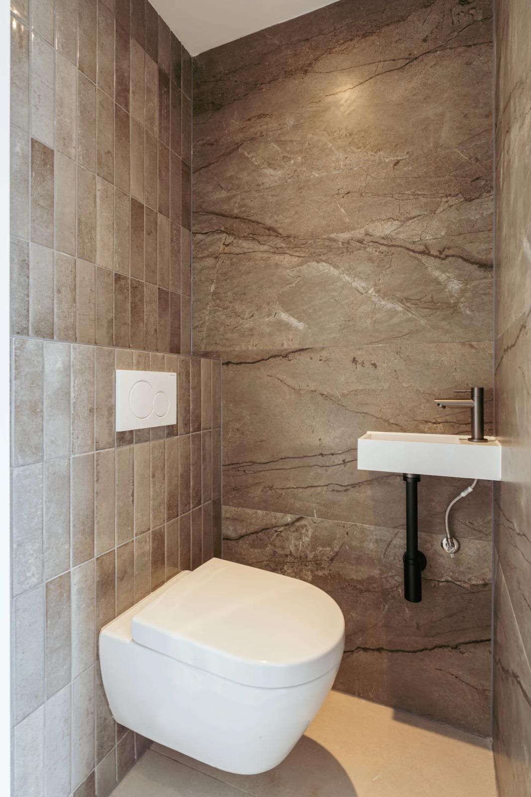 Toilet met marmerlook-wand en wand-wastafel.