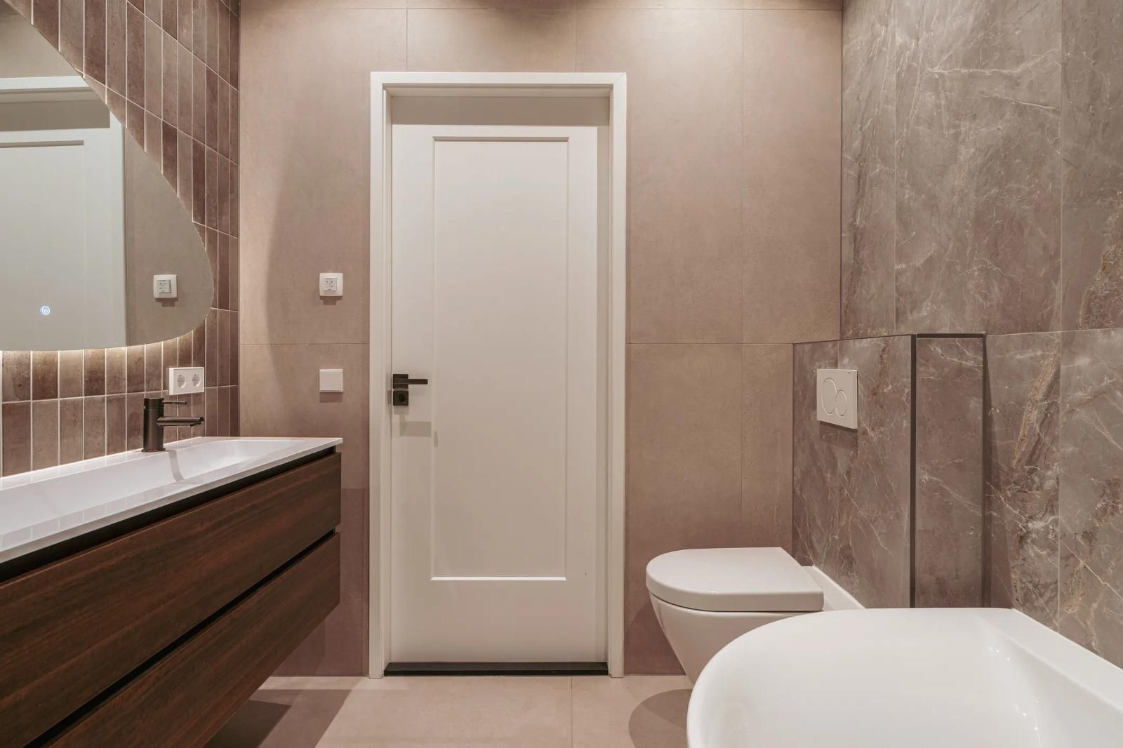 Moderne badkamer met marmerlook-tegels, houten wastafelmeubel en vrijstaand bad.