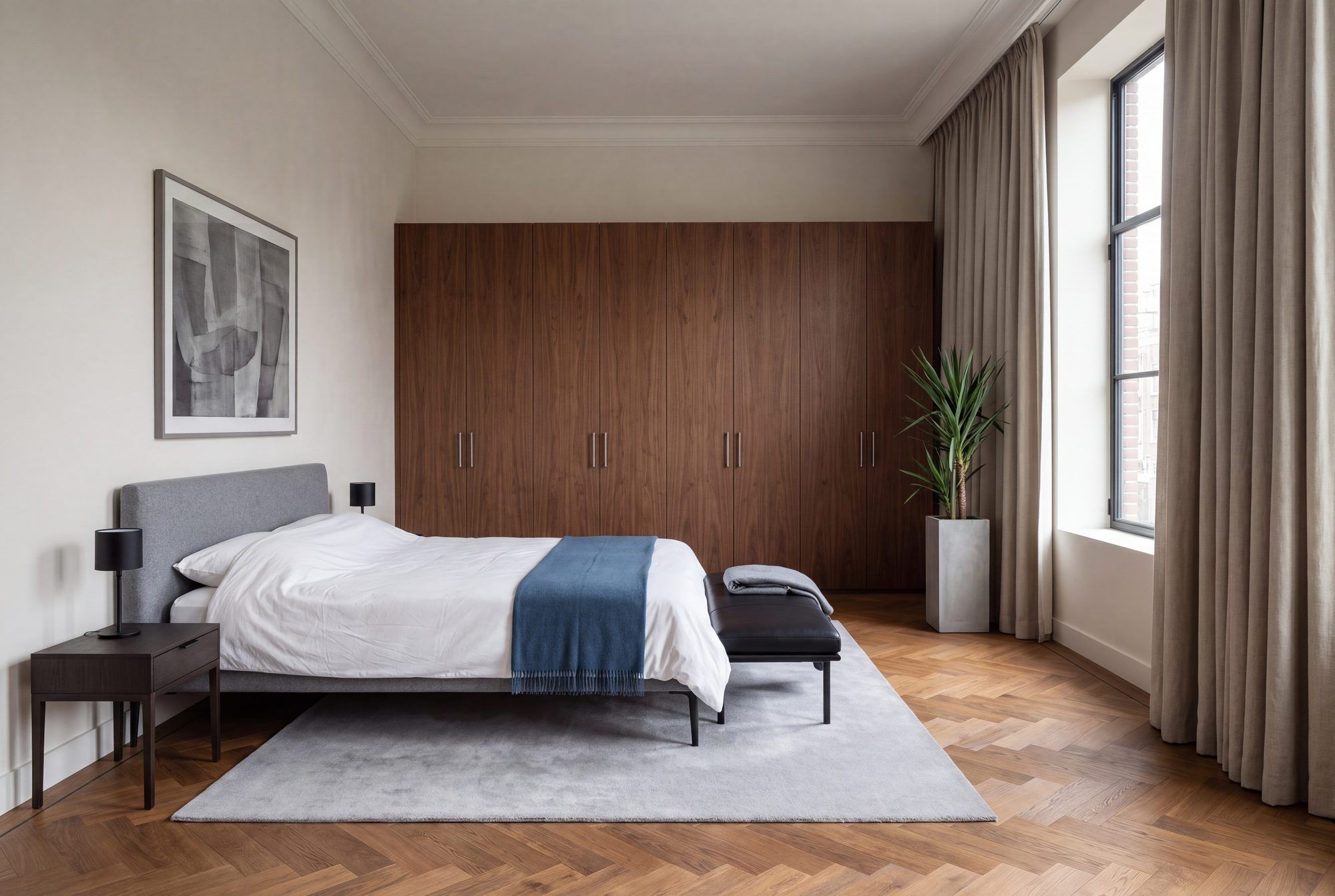 Slaapkamer met een gestoffeerd bed, twee nachtkasten en strak lijnenspel in koele tinten.