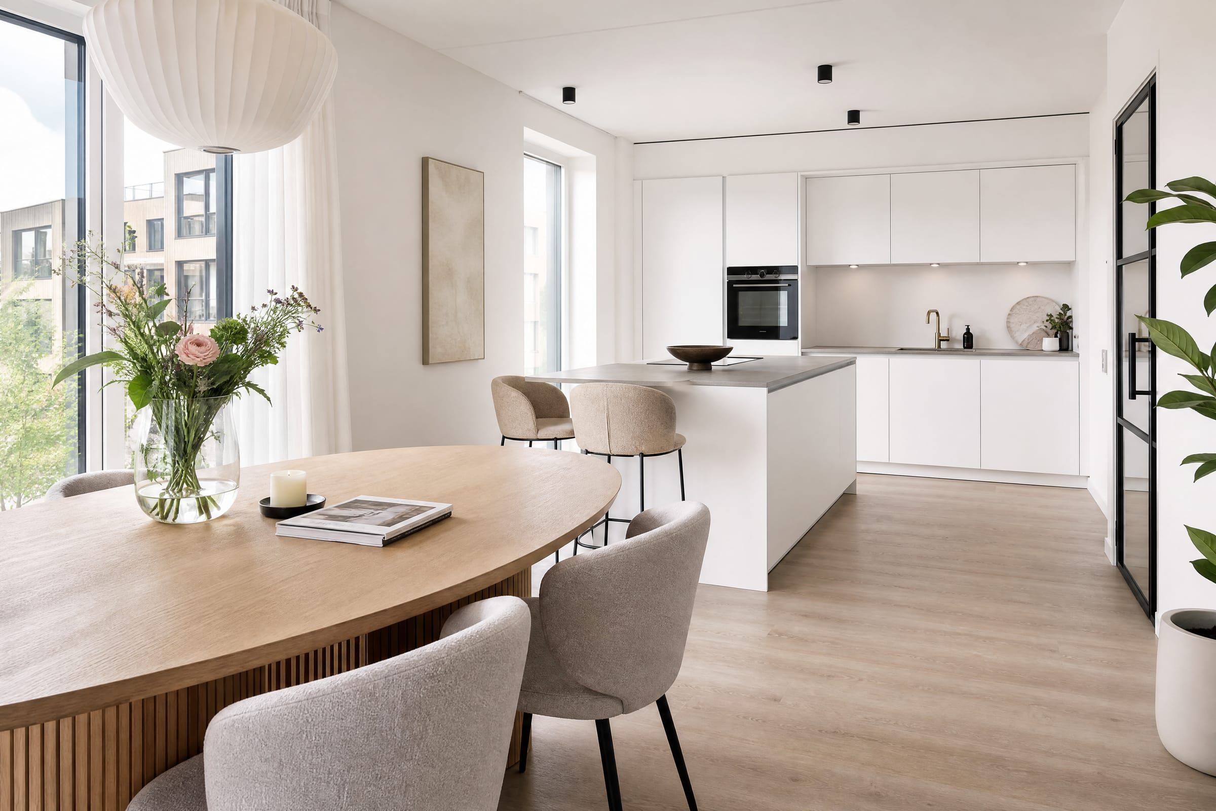 Woonkeuken met kookeiland, witte fronten en een ovale eettafel bij het raam.